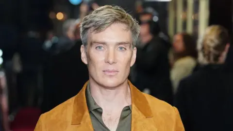 PA Media Cillian Murphy has short greyish hair and is wearing a mustard blazer and a light green shirt.